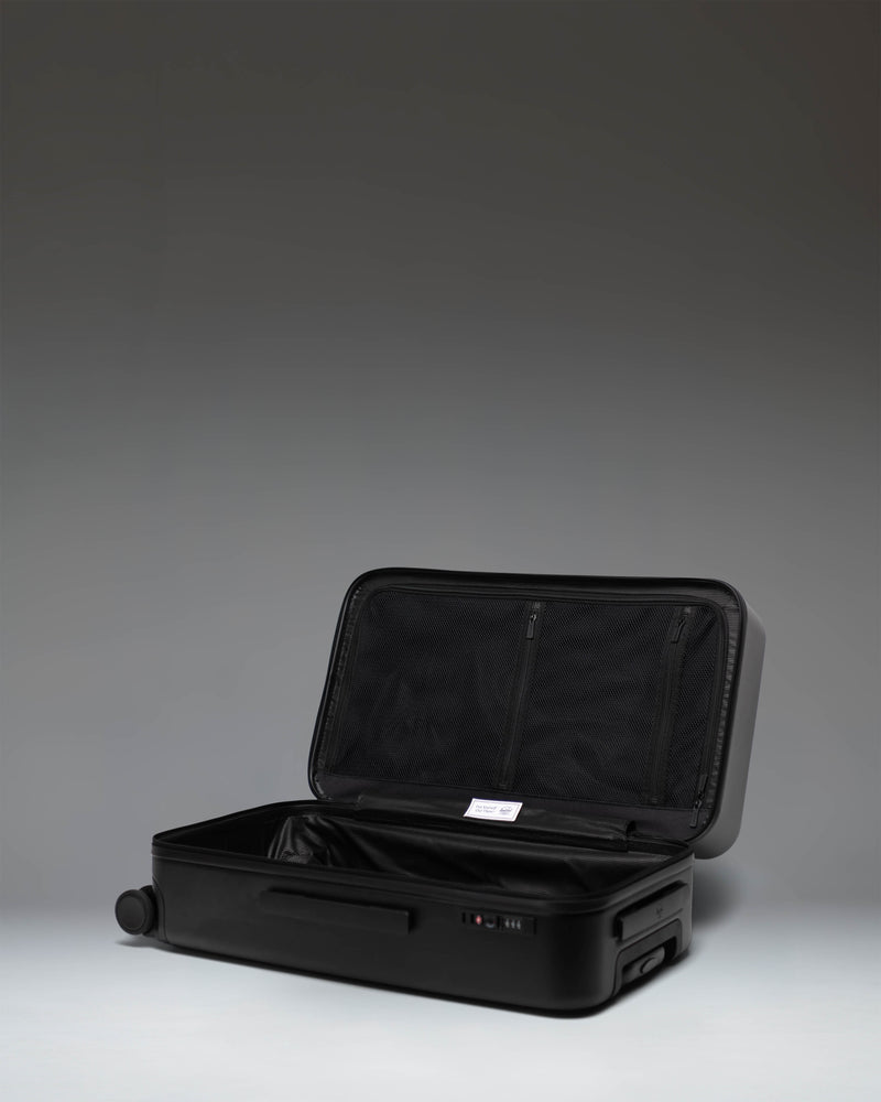 Black Herschel Heritage Hardshell Medium Luggage bag shown from a side profile view, highlighting its durable exterior.