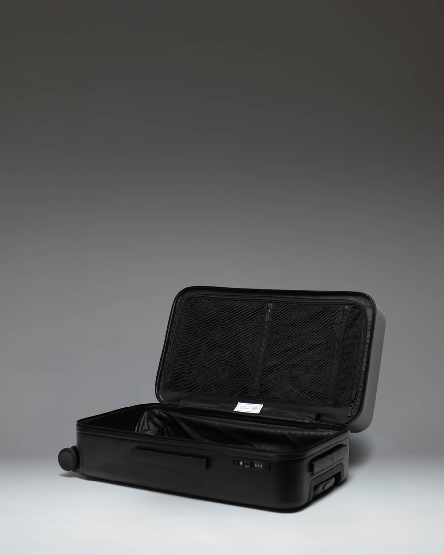 Black Herschel Heritage Hardshell Medium Luggage bag shown from a side profile view, highlighting its durable exterior.