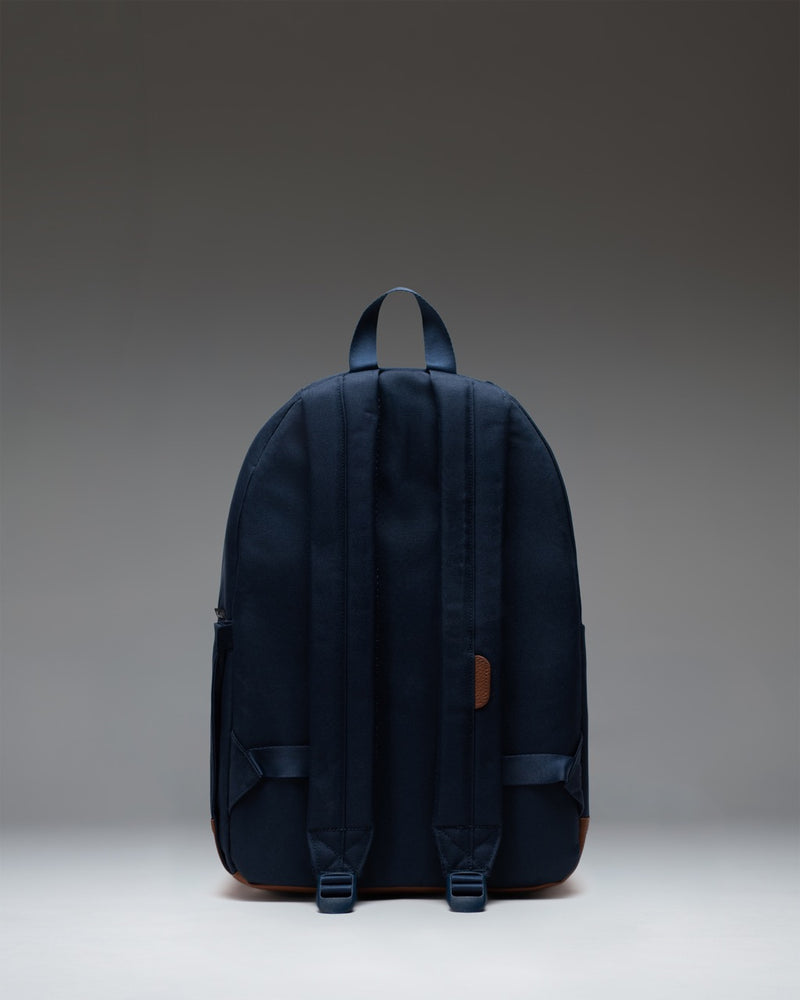 Herschel Supply Co. Pop Quiz Backpack in Navy blue with a brown tan faux leather bottom base, featuring a front zipper pocket with a white logo.