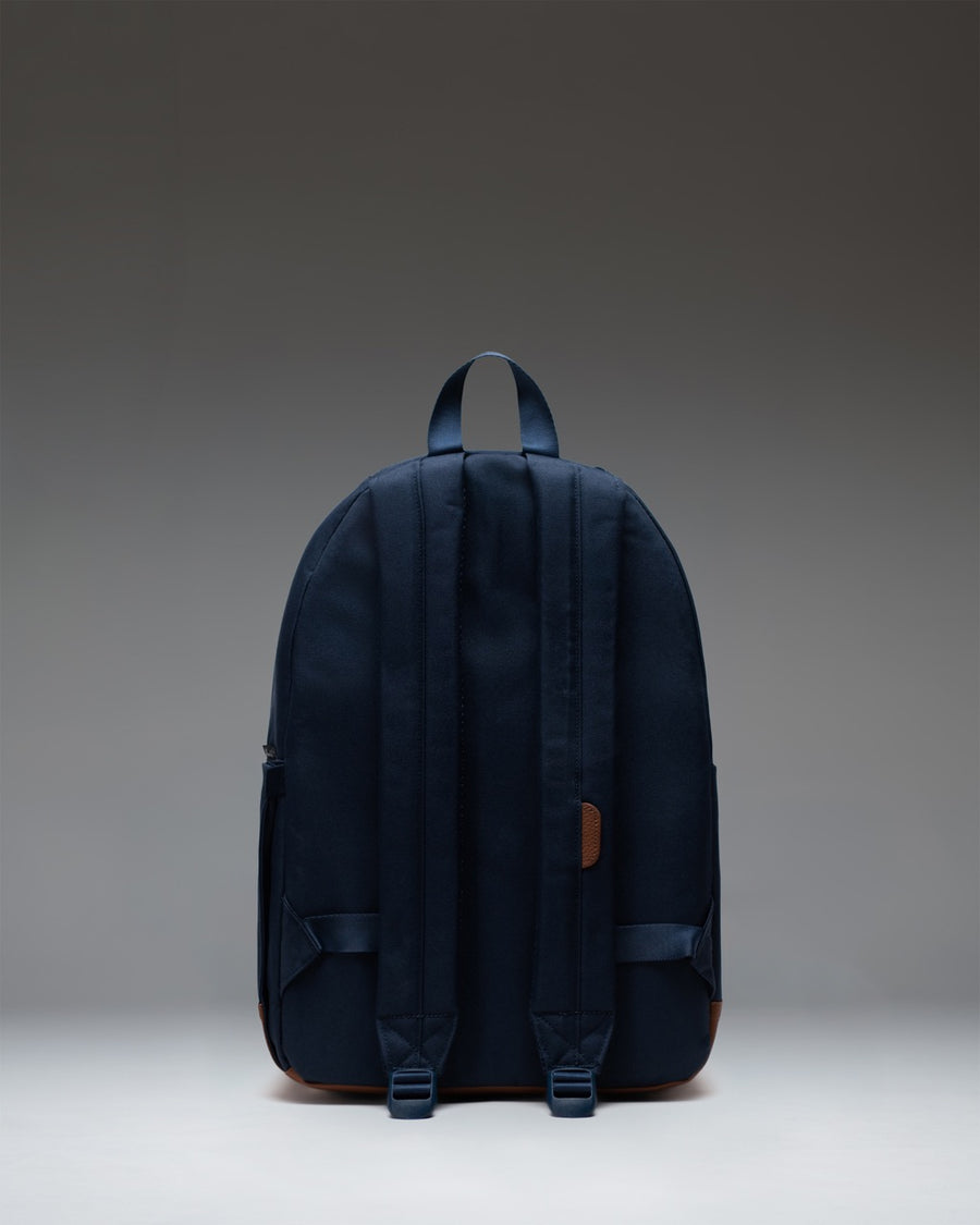 Herschel Supply Co. Pop Quiz Backpack in Navy blue with a brown tan faux leather bottom base, featuring a front zipper pocket with a white logo.