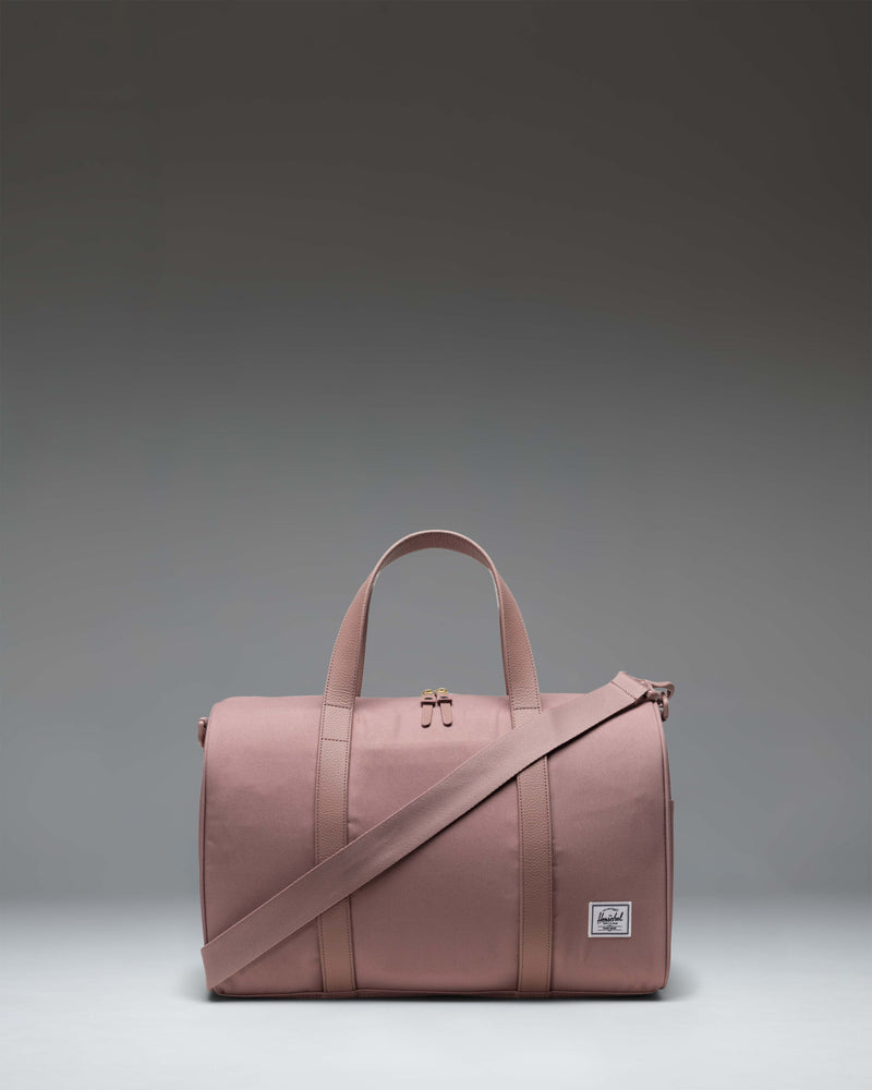 Herschel Supply Co. Novel Carry On Duffle bag in Ash Rose, a soft pink duffel with top handles and a removable shoulder strap.