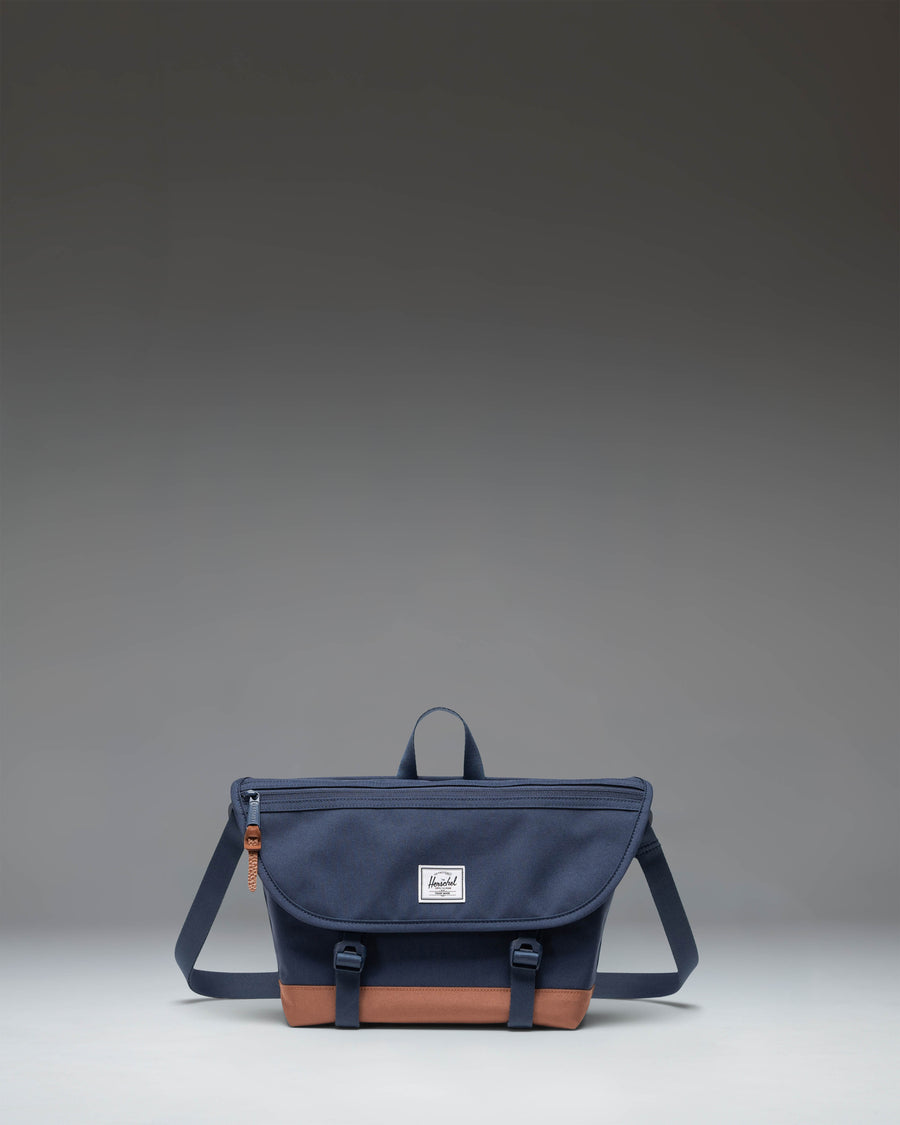 Herschel Supply Co Cove Small Messenger bag in Navy and Saddle Brown, showing a front view with the main flap and strap.