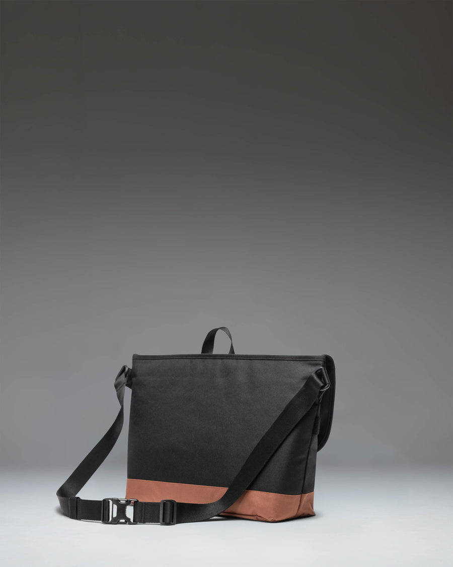Herschel Supply Co. Cove Messenger bag in Black/Saddle Brown featuring a front flap closure and a contrasting brown shoulder strap base.