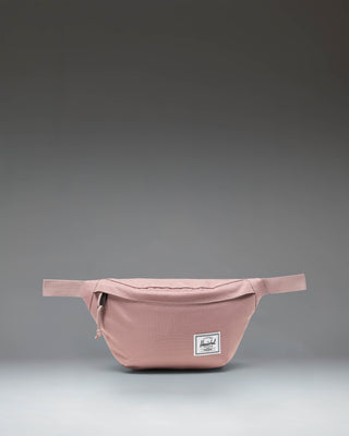 Herschel Classic Hip Pack in Ash Rose pink, featuring a front zippered pocket and an adjustable webbed strap with a buckle closure.