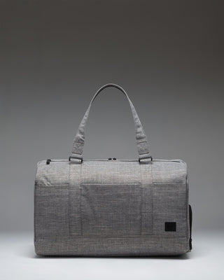 Herschel Novel Duffle Tech bag in Raven Crosshatch grey, showing a side view of the tech compartments and handles.