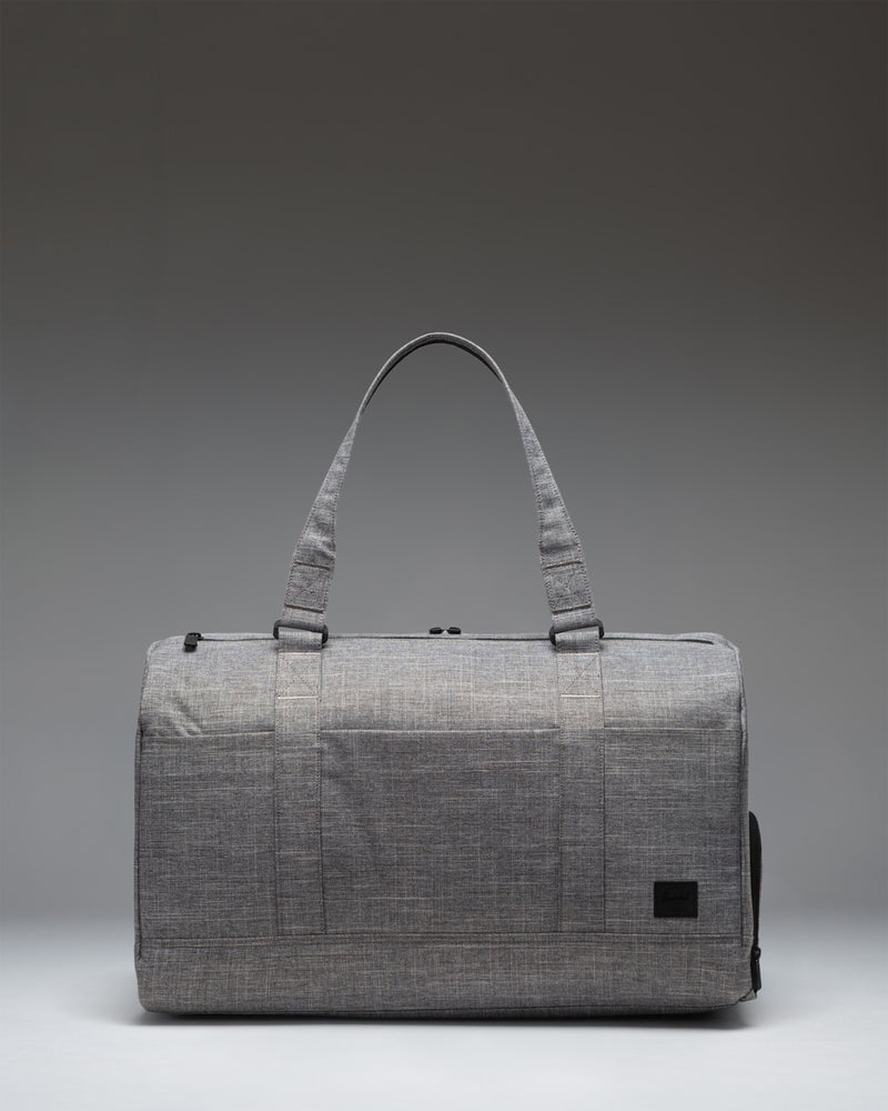 Herschel Novel Duffle Tech bag in Raven Crosshatch grey, showing a side view of the tech compartments and handles.