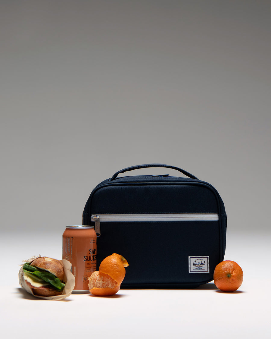 Herschel Supply Co. Pop Quiz Lunch Box in navy blue, showing the front view with a zipper pocket and classic white logo patch.