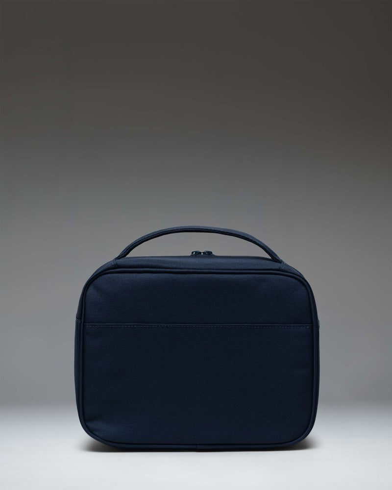 Herschel Supply Co. Pop Quiz Lunch Box in navy blue, showing an angled front view with the signature woven label and front pocket.
