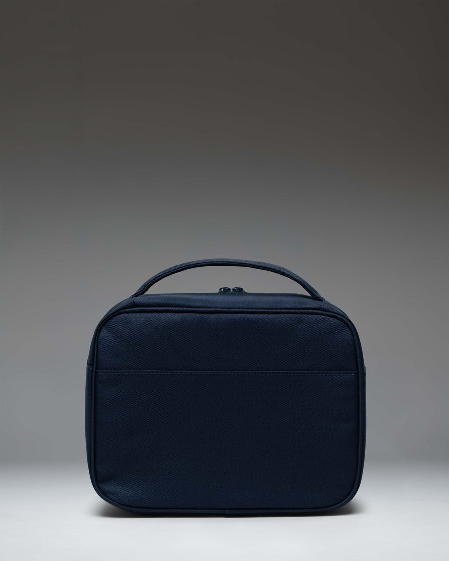Herschel Supply Co. Pop Quiz Lunch Box in navy blue, showing an angled front view with the signature woven label and front pocket.