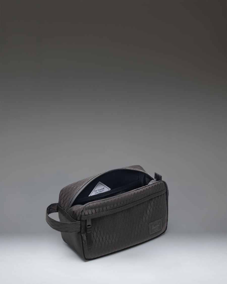 Herschel Supply Co. Chapter Travel Kit in Black Diamond/Black featuring a grid patterned material with a front zippered pocket and carrying handle.