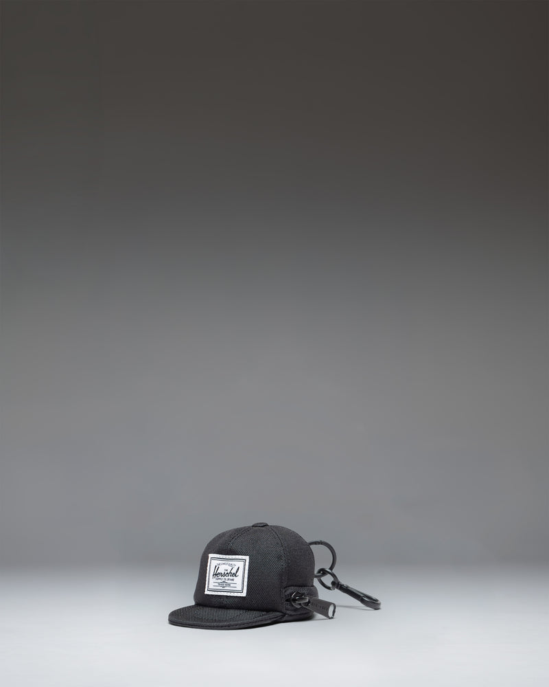 Herschel Supply Co. Sylas Classic Cap Bag Charm in black, showing the front view of a miniature baseball cap keychain accessory.