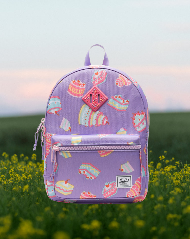 Herschel Heritage Kids Backpack in Cakes, a light pink backpack with a playful colorful cake and cupcake print.