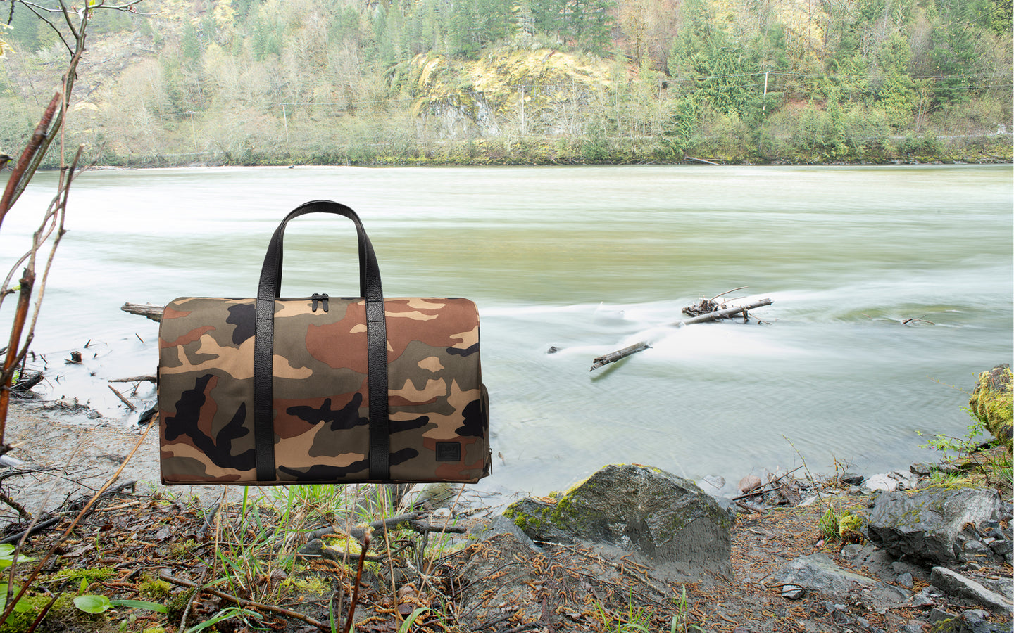 Herschel Novel Duffle bag in Woodland Camo with black accents and a Black Label logo, shown from the side against a neutral background.