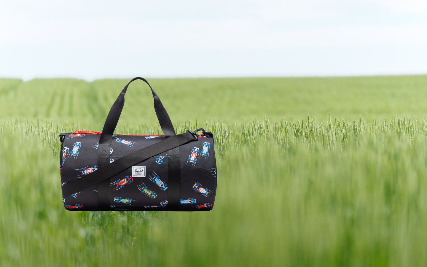 Herschel Classic Duffle Little Herschel in Race Cars print, featuring a pattern of colorful race cars on a dark background.
