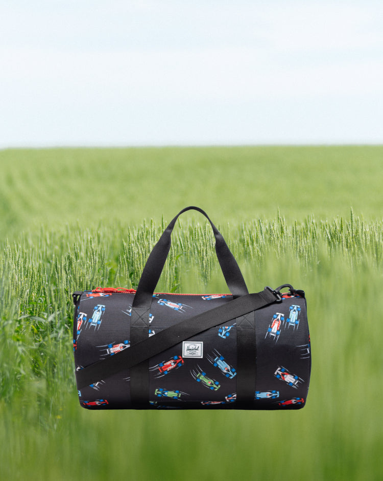 Herschel Classic Duffle Little Herschel in Race Cars pattern, featuring a colorful toy car print on a dark background.