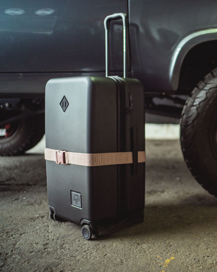 Herschel Supply Co. adjustable luggage belt in Ash Rose pink colorway, featuring a secure buckle clasp and signature classic woven label.