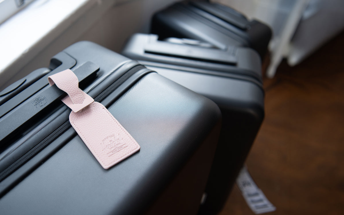 Herschel Supply Co. vegan leather luggage tag in Ash Rose pink, featuring an adjustable strap with a gold-tone buckle.