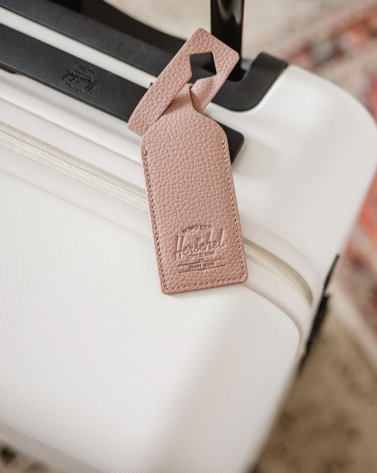 Herschel Supply Co. vegan leather luggage tag in Ash Rose pink with an adjustable strap, ideal for travel bags and suitcases.