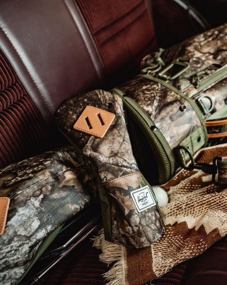Herschel Supply Co. x Realtree collection bags and accessories displayed together in the Realtree APX camouflage pattern.