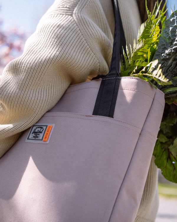 A Herschel Supply Alexander Zip Tote Insulated in Ash Rose on someone's shoulder with a variety of fresh vegetables sticking out of it